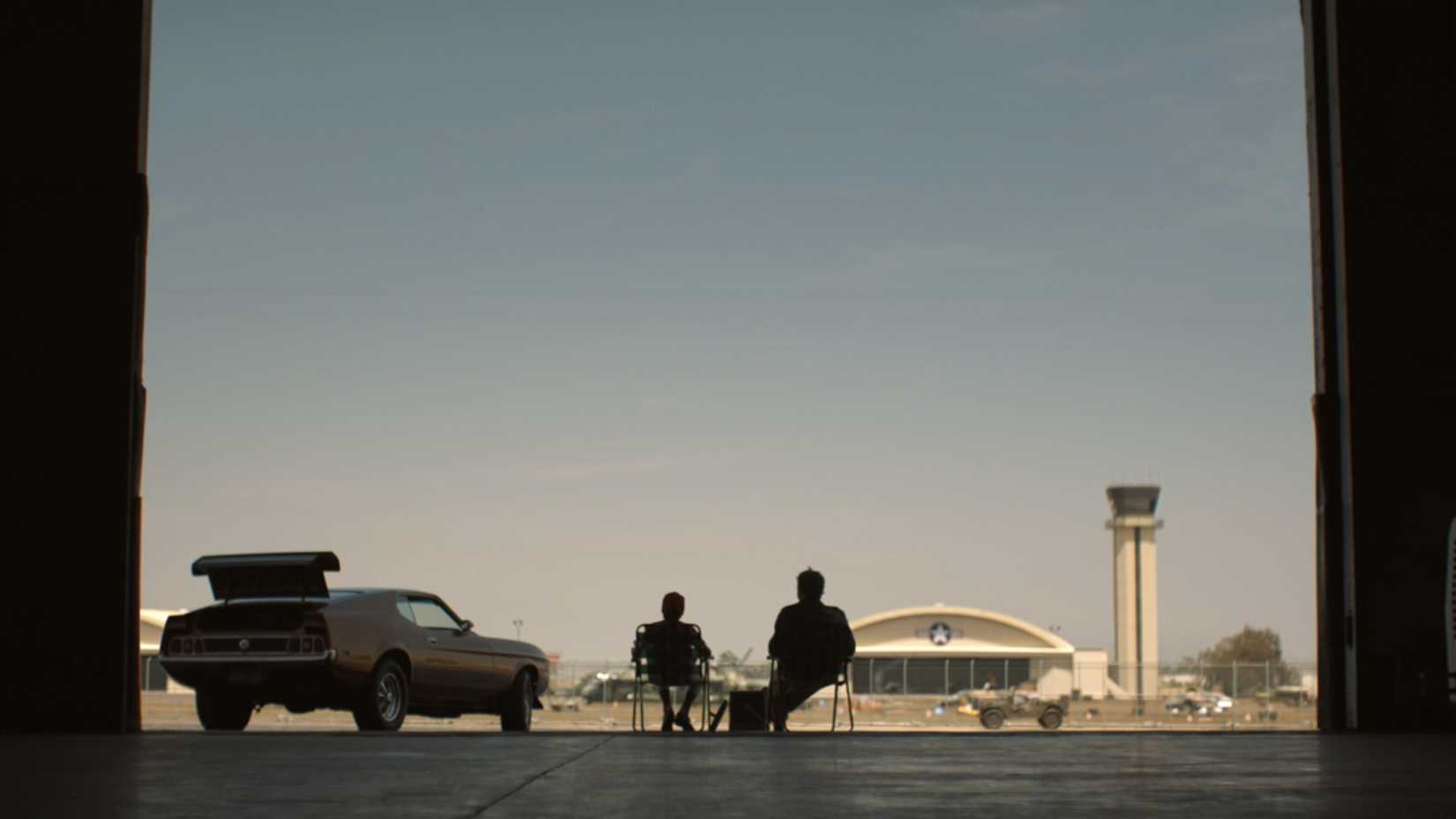 Martin Jordan e o jovem Hal sentados diante do hangar de uma base de aeronaves em cena do episódio 7 de Lanternas