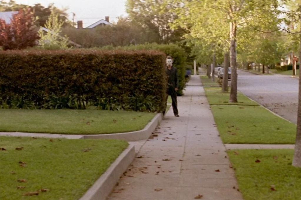 Michael Myers observa uma rua de Haddonfield atrás de uma cerca viva em Halloween, de 1978.